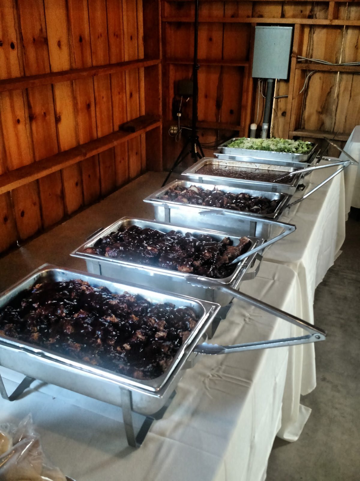 Barn wedding buffet line — chafing pans of glazed ribs, chicken, beans, and salad