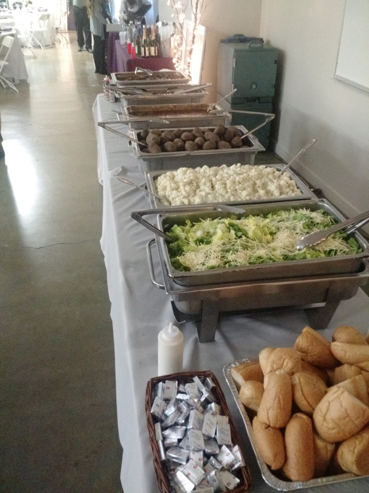 White-linen wedding buffet line with caesar salad, potato salad, and rolls